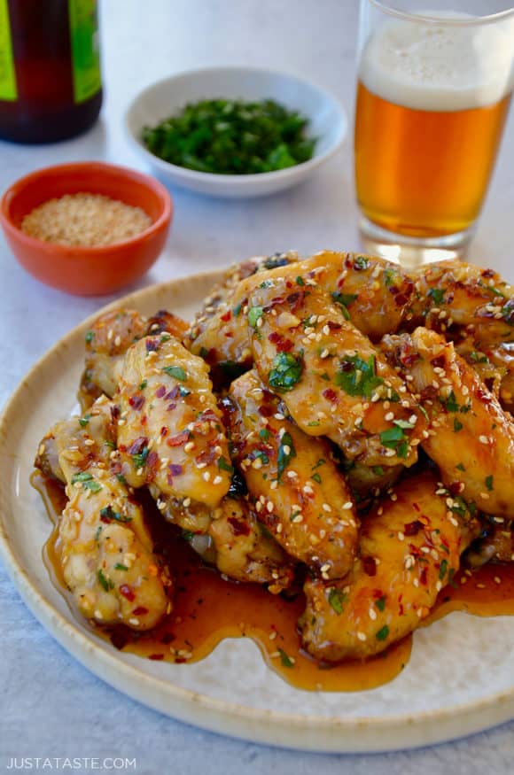 A white plate containing chicken wings with sesame seeds, cilantro and a beer in the background