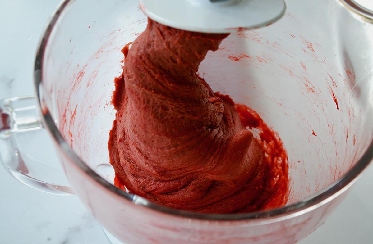 Red velvet cinnamon roll dough is being mixed in a stand mixer fitted with a dough hook.