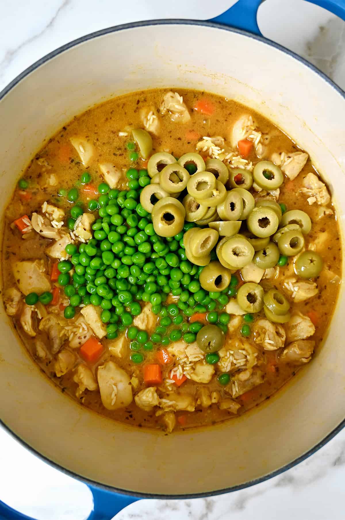 Sliced green olives and frozen peas with cooked chicken thighs and chicken stock in a Dutch oven.