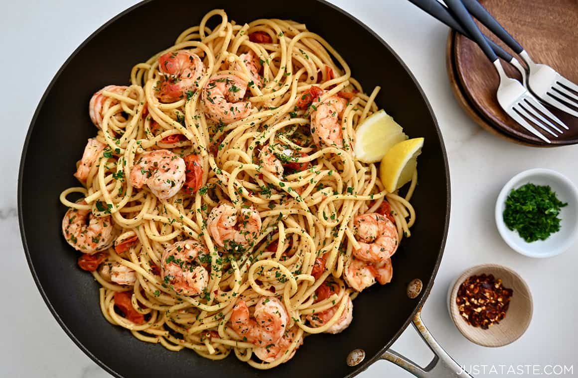 The best shrimp scampi in a skillet with lemon wedges next to two small bowls containing fresh herbs and crushed red pepper