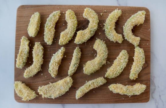 Slices of breaded avocado on wood cutting board