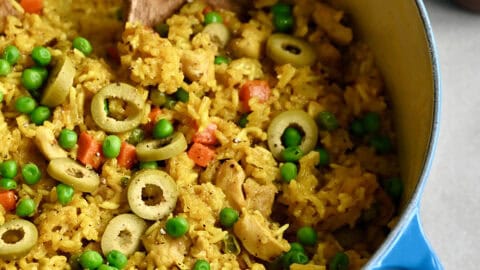 One-Pot Chicken and Yellow Rice Cuban-style with peas, carrots, onions and green olives in a Dutch oven.