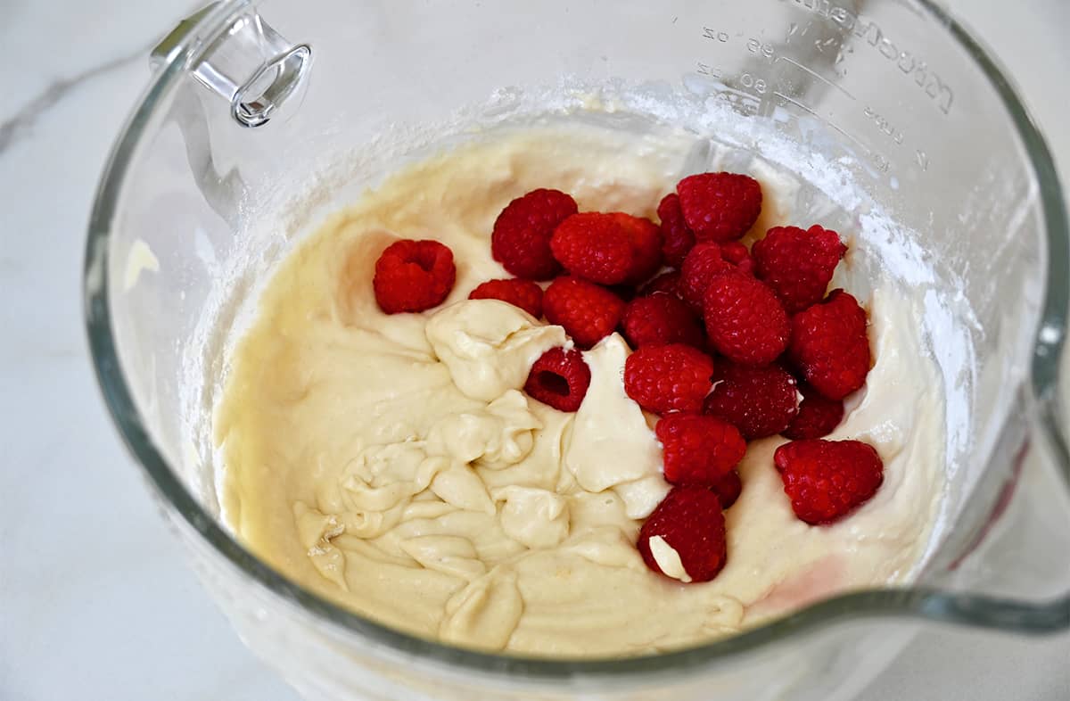 Stand mixer bowl containing coffee cake batter topped with fresh raspberries.