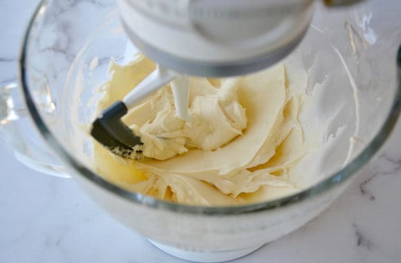 A clear stand mixer bowl filled with cream cheese frosting