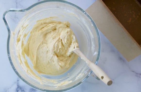 Mixing bowl with spatula containing batter next to parchment paper lined loaf pan