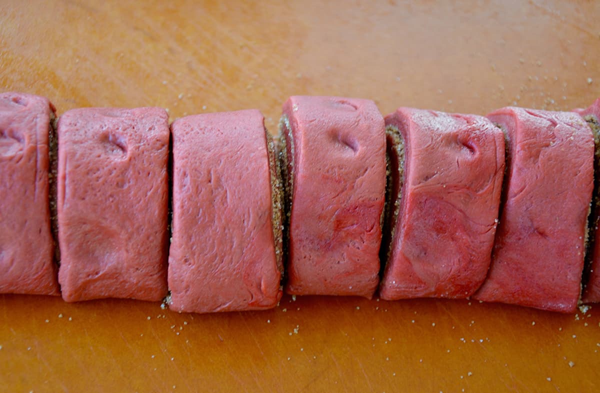 Just-cut slices of red velvet cinnamon rolls sit on a cutting board.