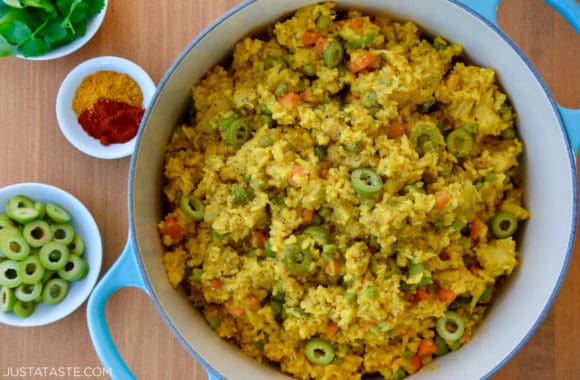 One Pot Chicken and Yellow Rice next to small bowls containing sliced green olives, spices and herbs