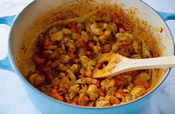 Dutch oven containing cubed chicken thighs, vegetables and wooden spoon