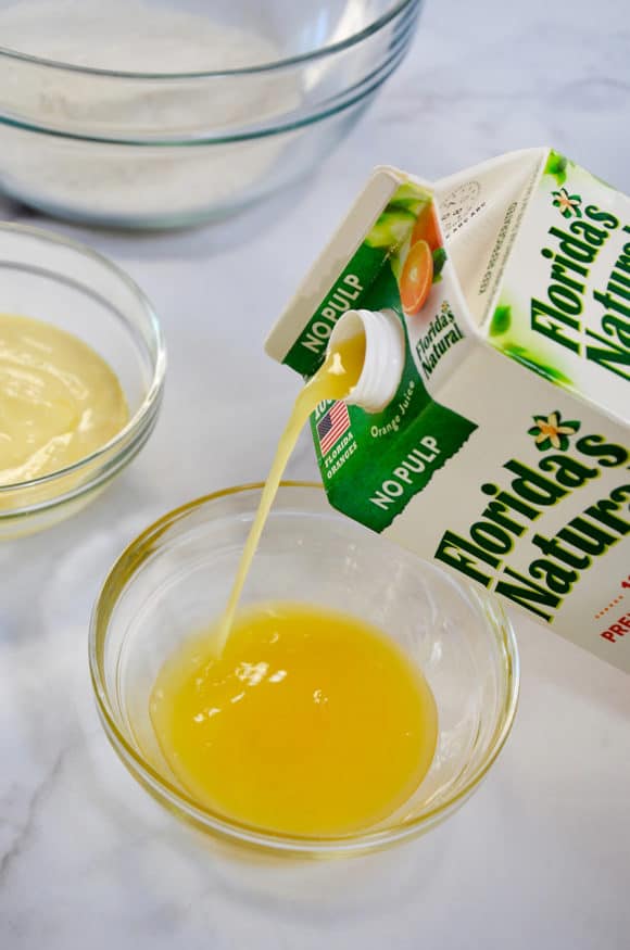 Carton of orange juice being poured into a glass bowl