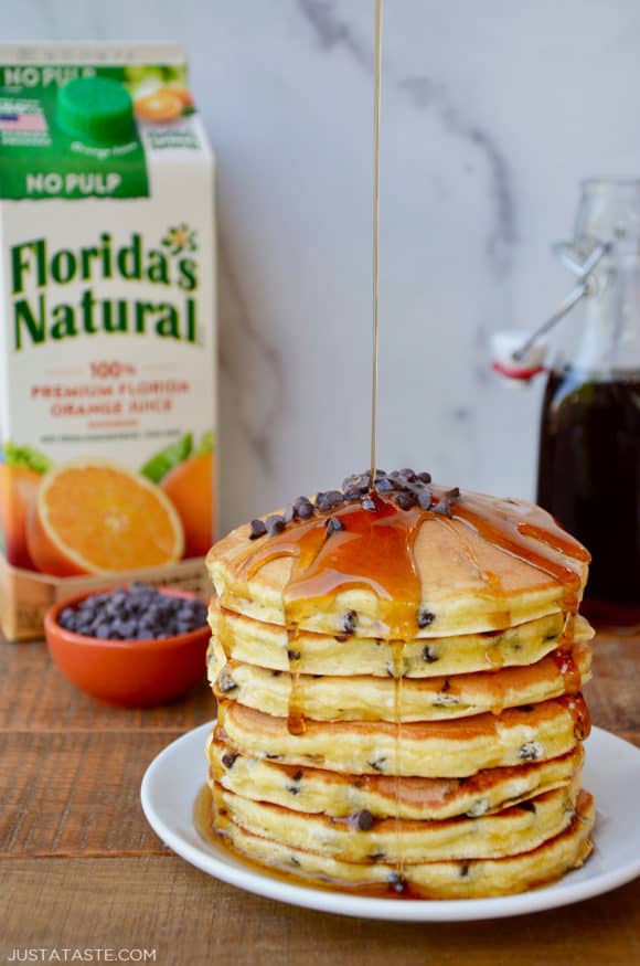 Stack of pancakes on a white plate with a carton of orange juice behind it