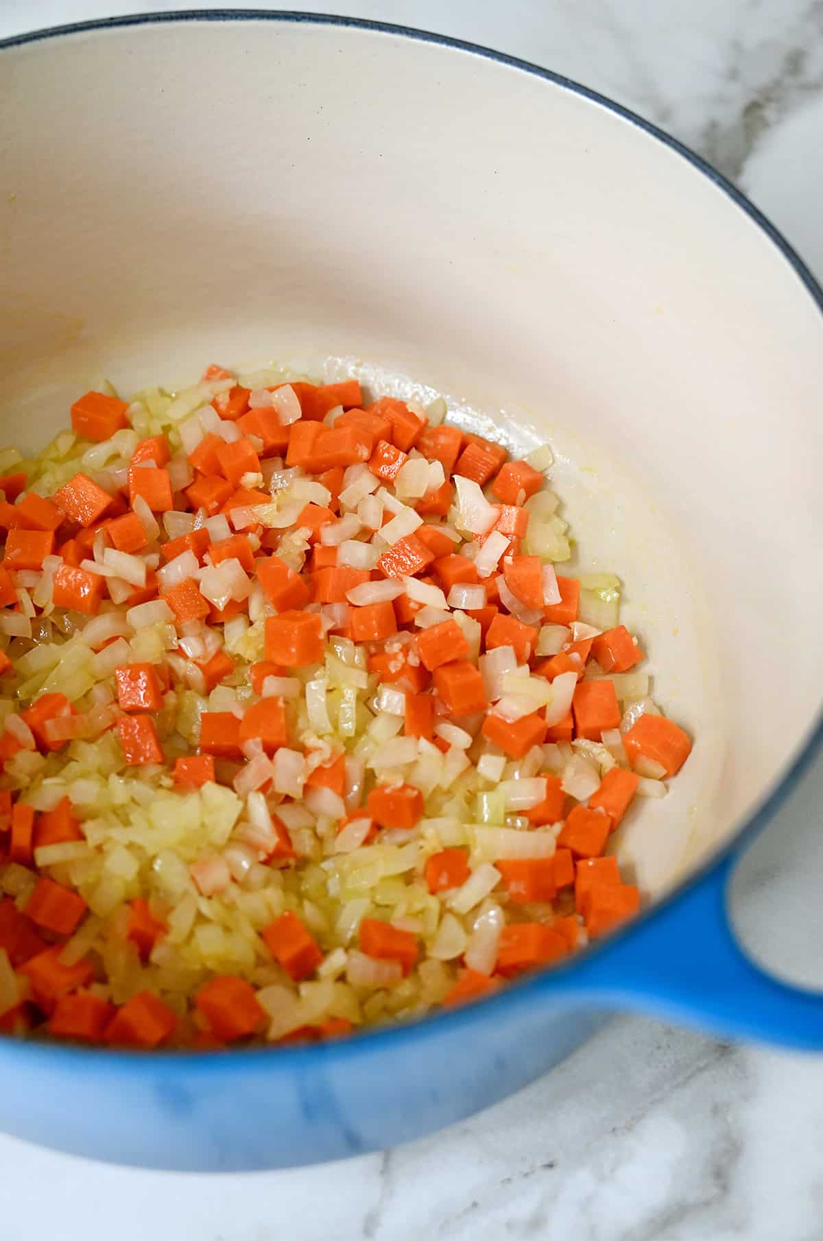 Sautéed diced carrots and onions in a blue Dutch oven.