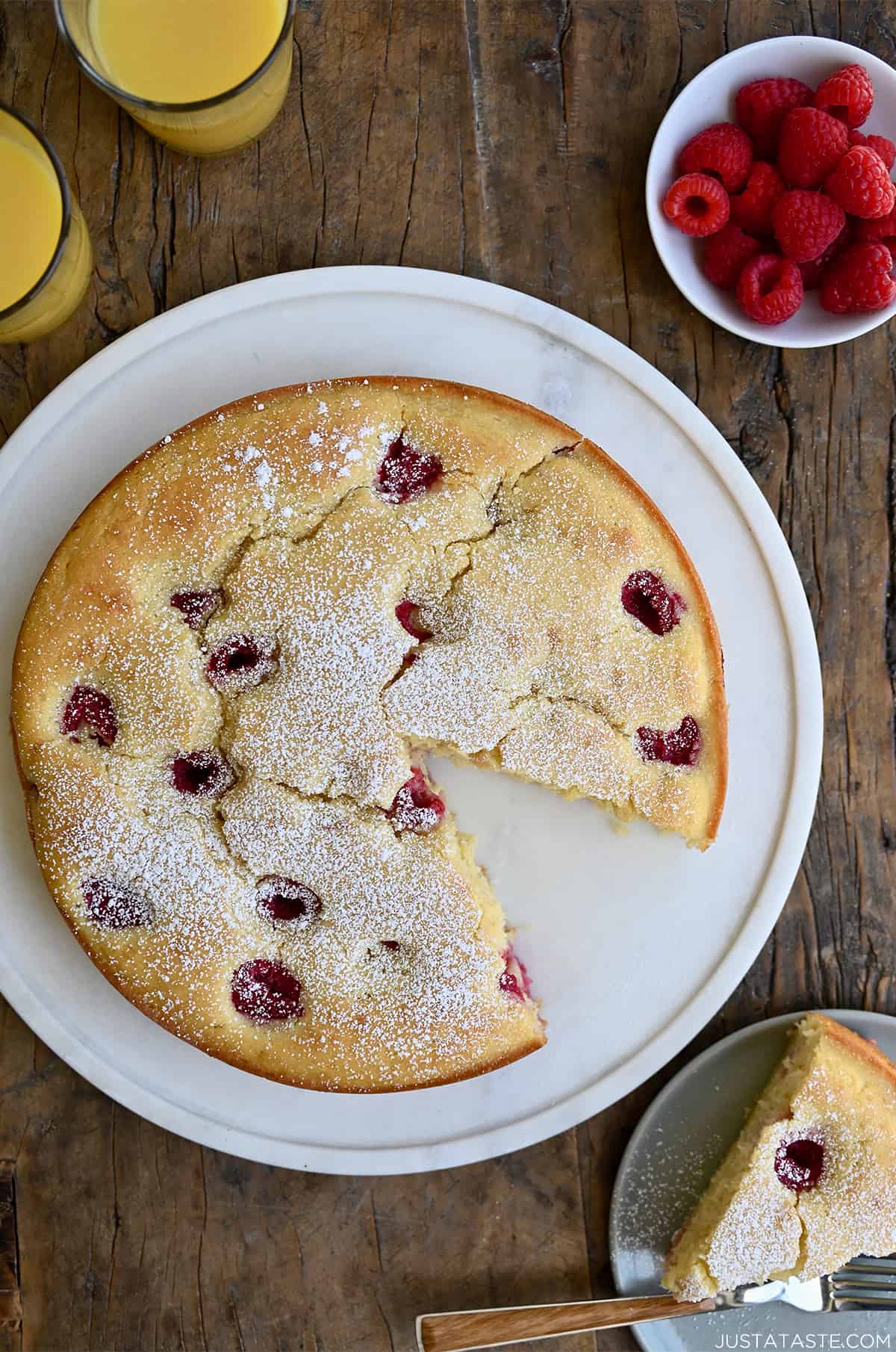 A round coffee cake studded with raspberries and dusted with powdered sugar on a serving platter.