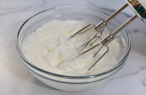 Egg whites being whipped with a handheld beater in a glass bowl