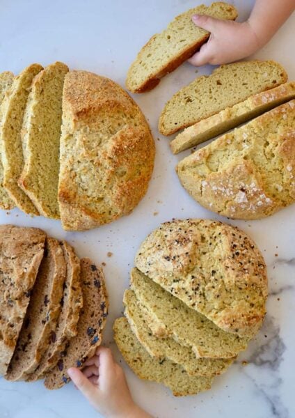 Four loaves of sliced bread with little kids hands grabbing slices