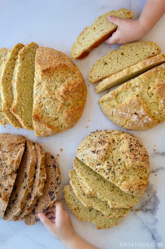 Four loaves of sliced bread with little kids hands grabbing slices