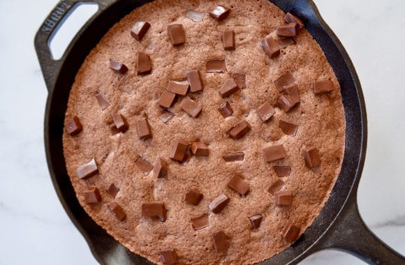 A cast-iron skilled with baked brownies topped with chocolate chunks