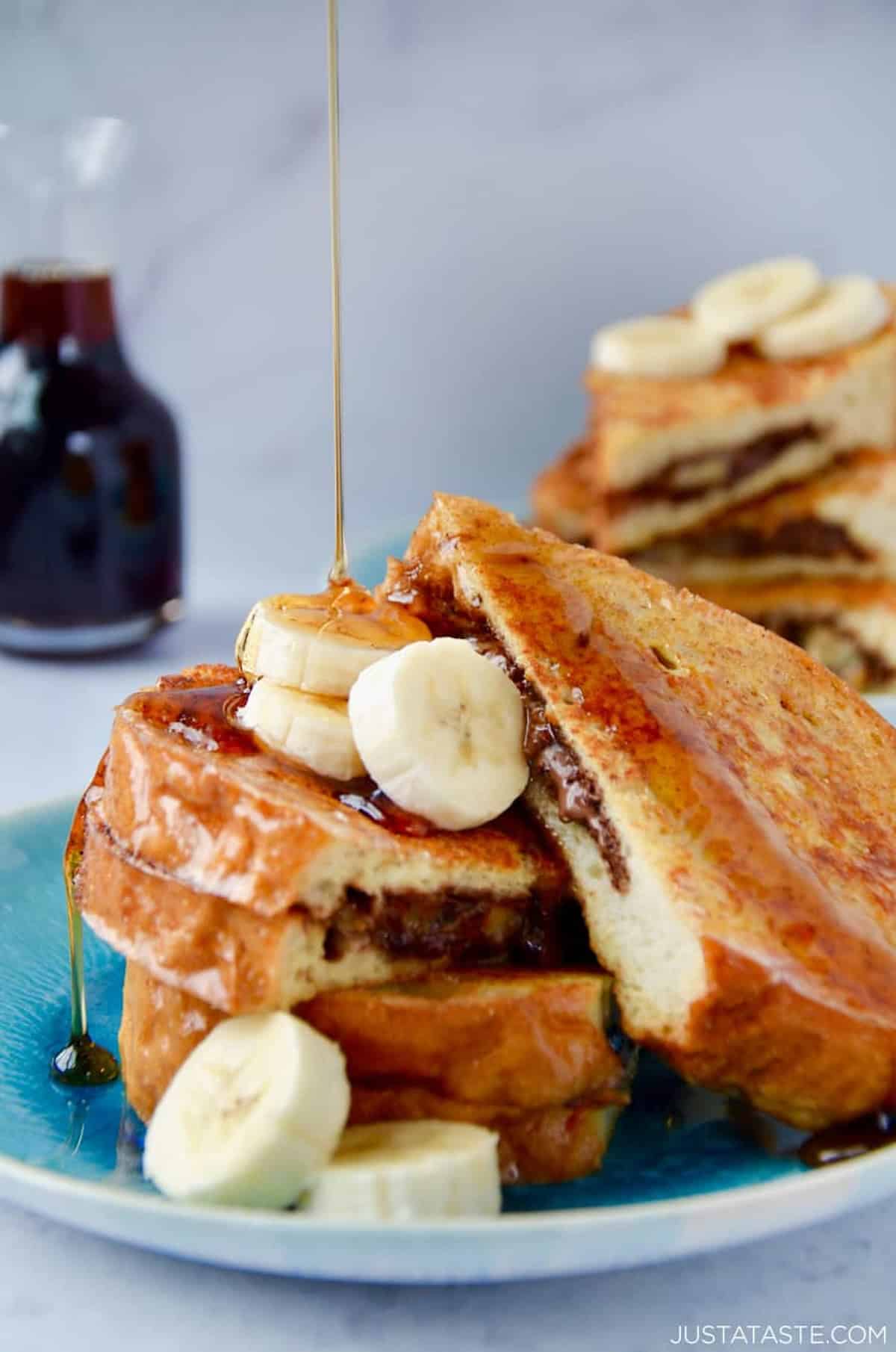 Stuffed French toast with Nutella and bananas drizzled with maple syrup on a plate.