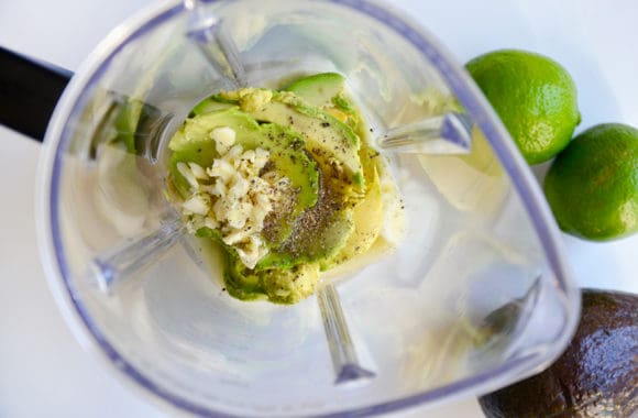 Top down view of blender containing yogurt, avocado, minced garlic, salt and pepper