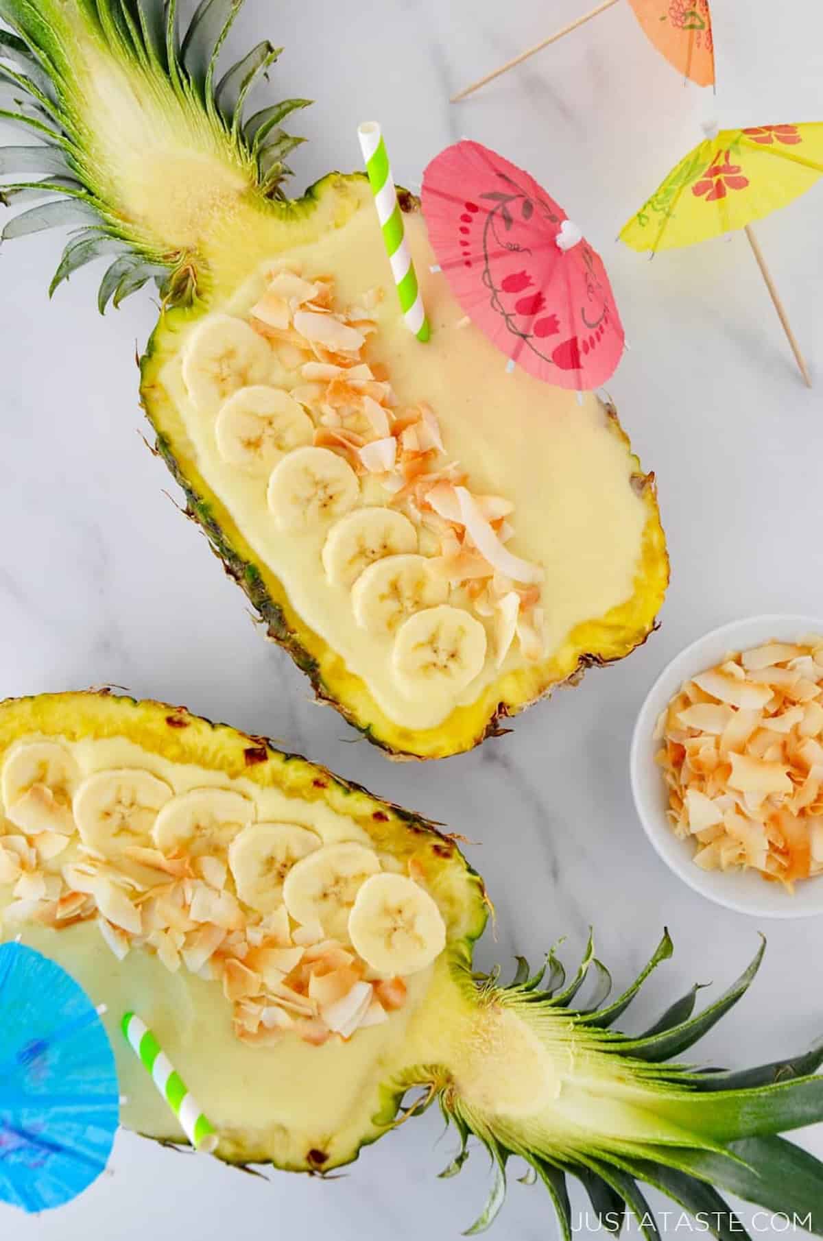 Creamy coconut pineapple smoothies in pineapple bowls with slices of banana and toasted coconut as garnishes.
