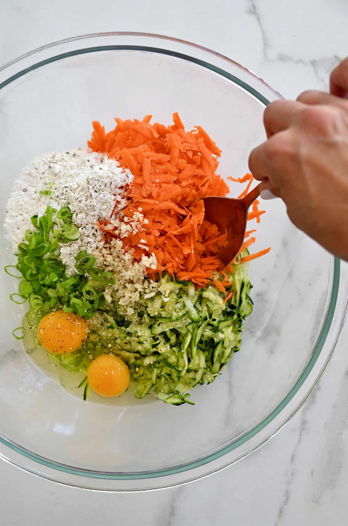 Shredded zucchini, flour, shredded carrots, eggs and chopped scallions in a mixing bowl.