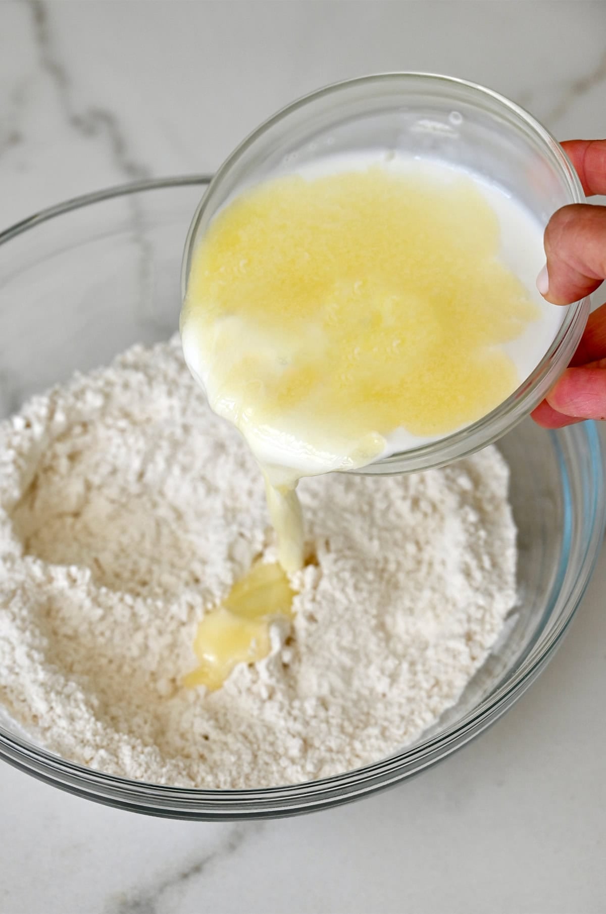 Pouring buttermilk and melted butter into a bowl with dry ingredients to make bread without yeast.