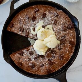 A cast-iron skillet brownie topped with ice cream and confectioners' sugar