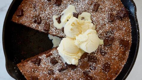 A cast-iron skillet brownie topped with ice cream and confectioners' sugar