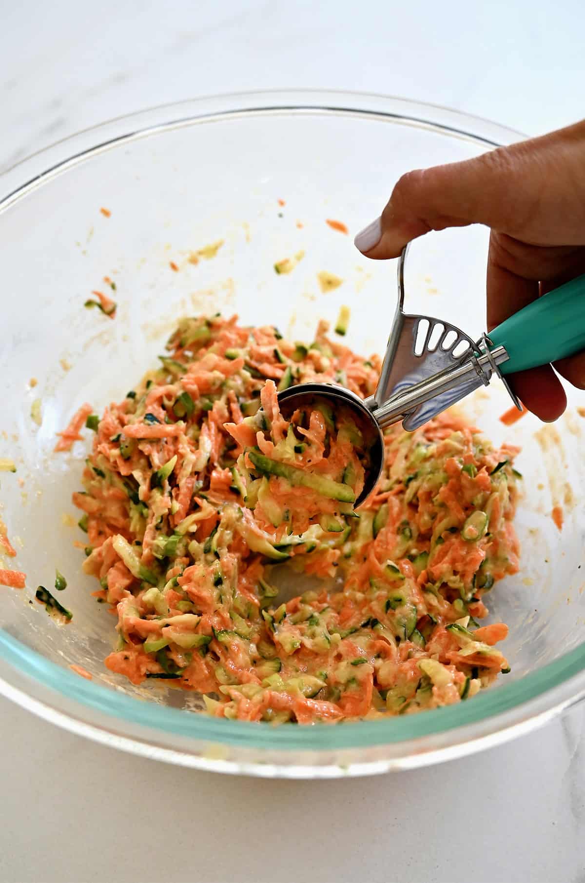Scooping vegetable fritter batter from a bowl with an ice cream scoop.