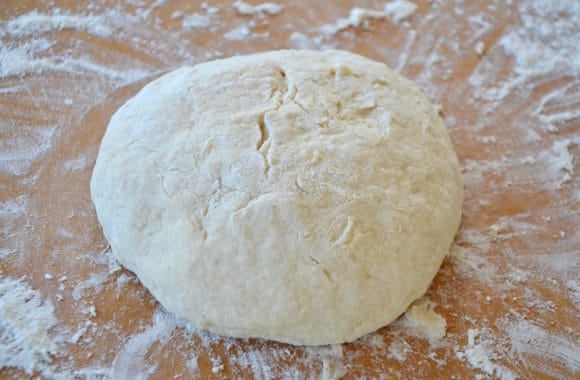 A ball of bread dough on a floured brown cutting board