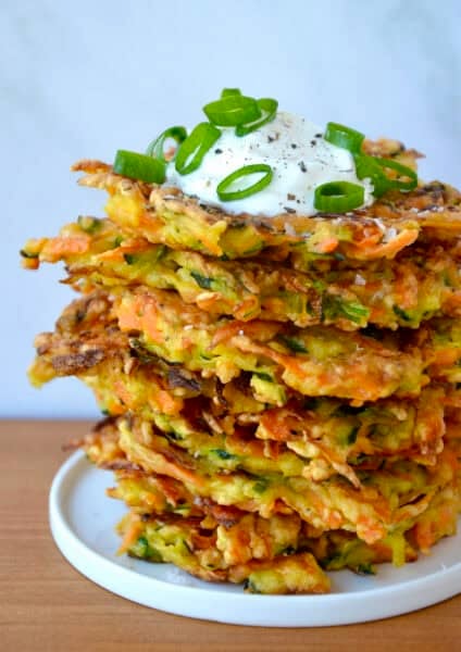 Stack of Quick and Crispy Vegetable Fritters topped with sour cream and sliced scallions.