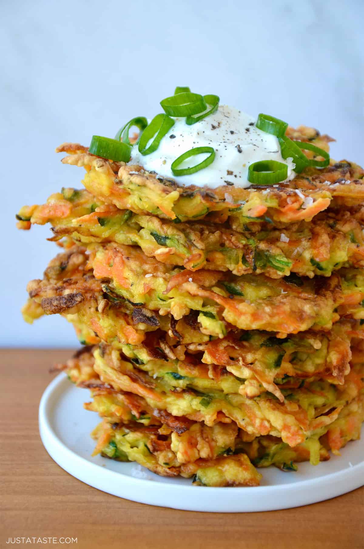 Stack of Quick and Crispy Vegetable Fritters topped with sour cream and sliced scallions.