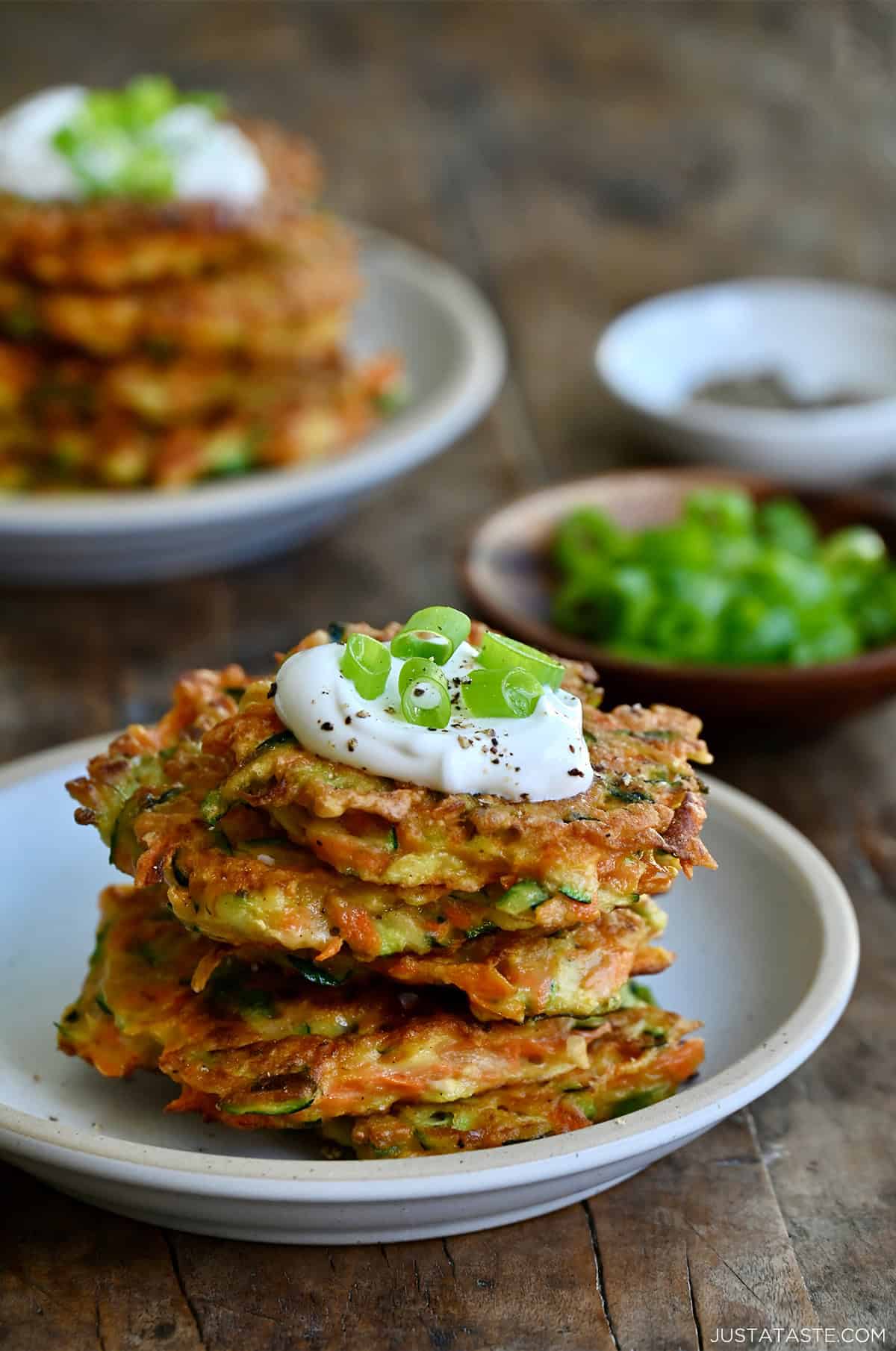 A tall stack of crispy vegetable fritters topped with a dollop of sour cream, salt, pepper and chopped green onions.