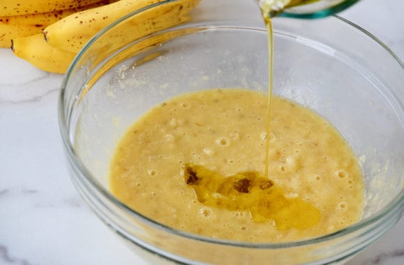 Olive oil being poured atop mashed bananas in glass bowl