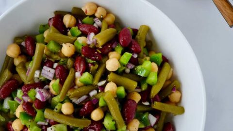 A white bowl containing three-bean salad with spoons and glasses next to it