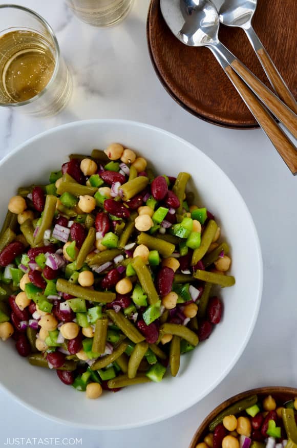 A white bowl containing three-bean salad with spoons and glasses next to it