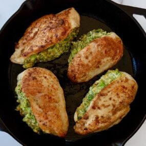 A cast-iron skillet containing seared, stuffed chicken breasts