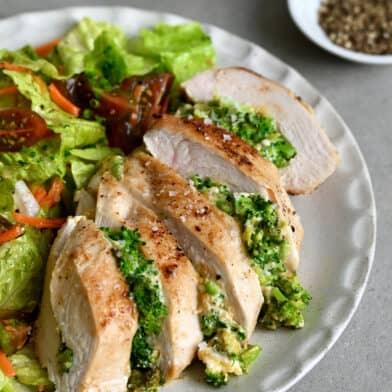 Broccoli and cheddar stuffed chicken breast on a dinner plate with a crisp green salad.