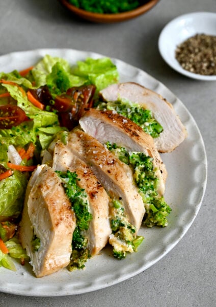 Broccoli and cheddar stuffed chicken breast on a dinner plate with a crisp green salad.