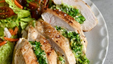 Broccoli and cheddar stuffed chicken breast on a dinner plate with a crisp green salad.