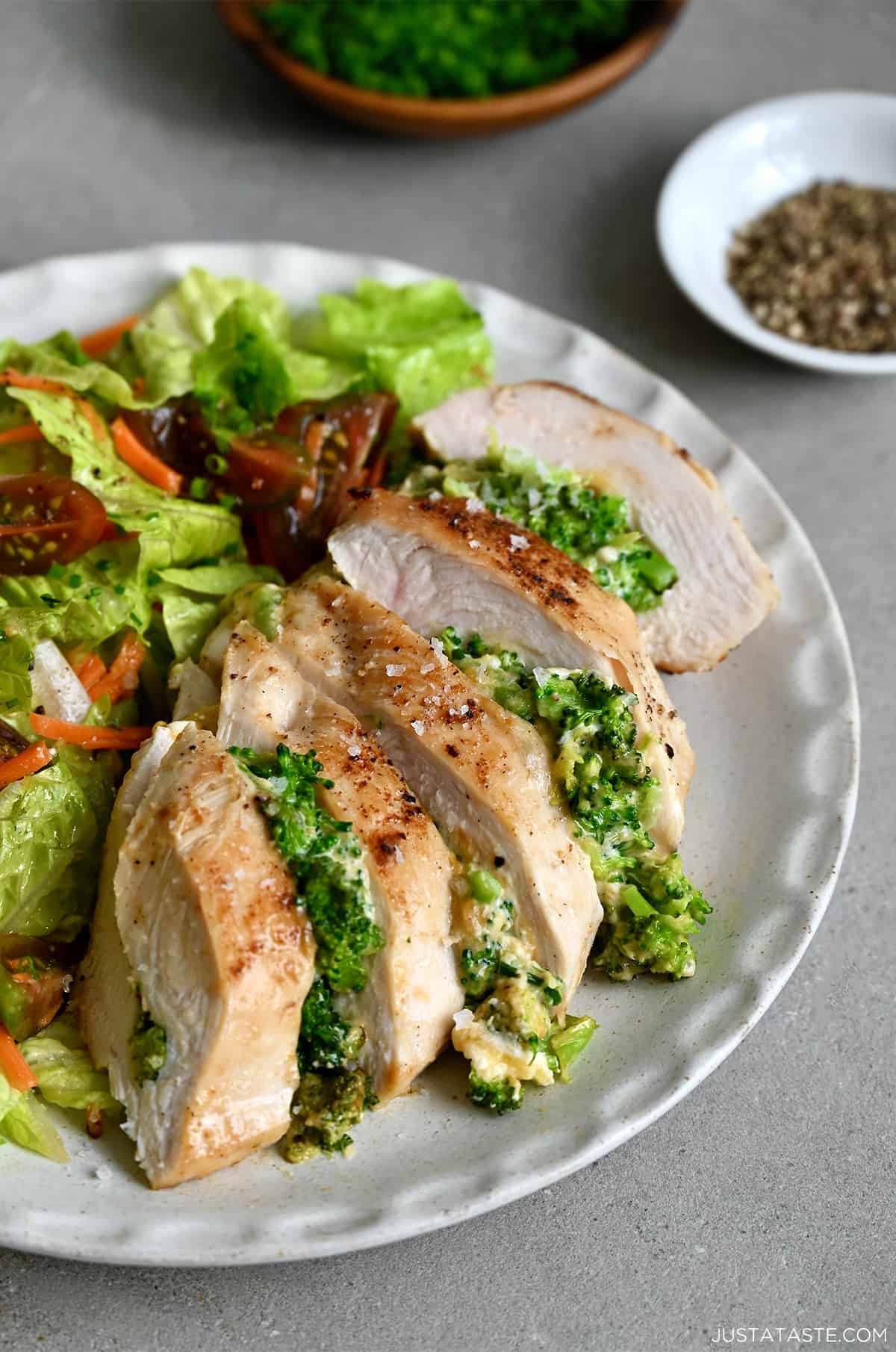 Broccoli and cheddar stuffed chicken breast on a dinner plate with a crisp green salad.