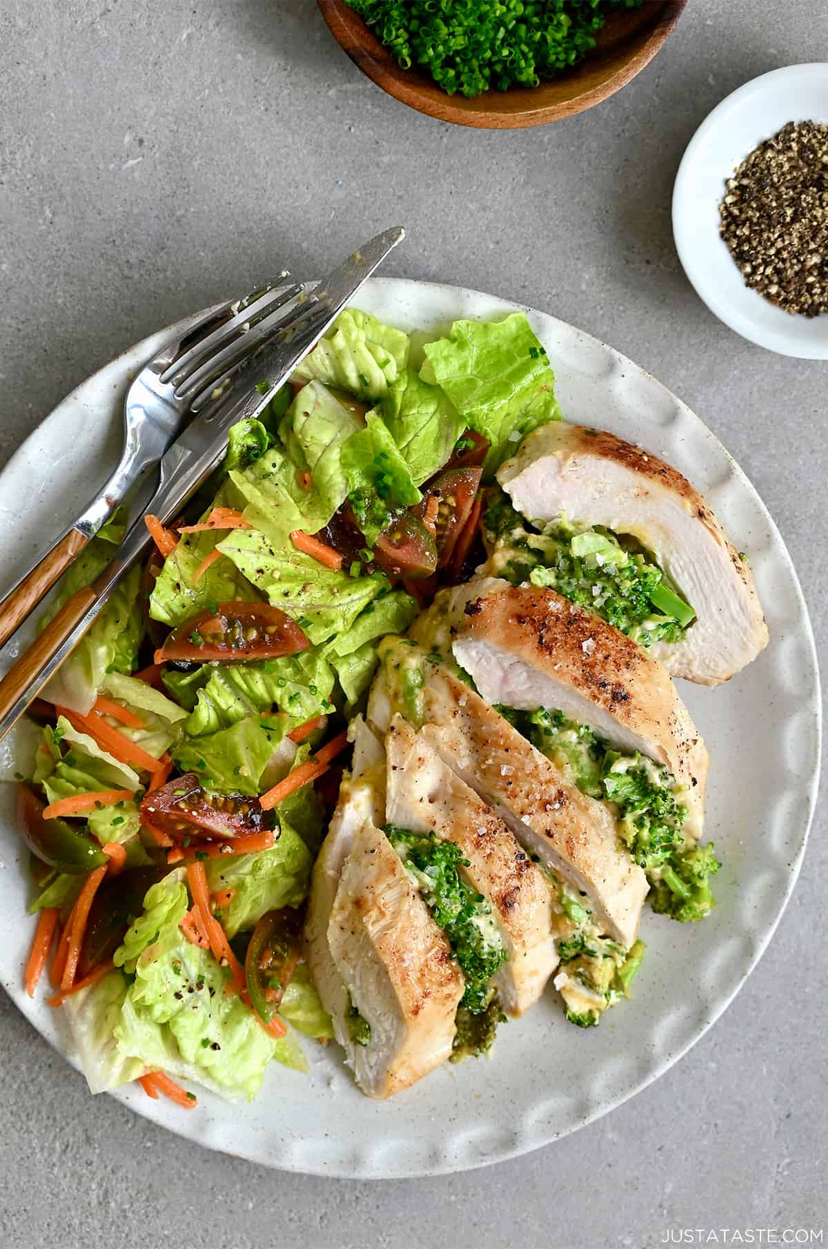 Broccoli and cheese stuffed chicken breast on a plate with a romaine lettuce salad, and a fork and knife.