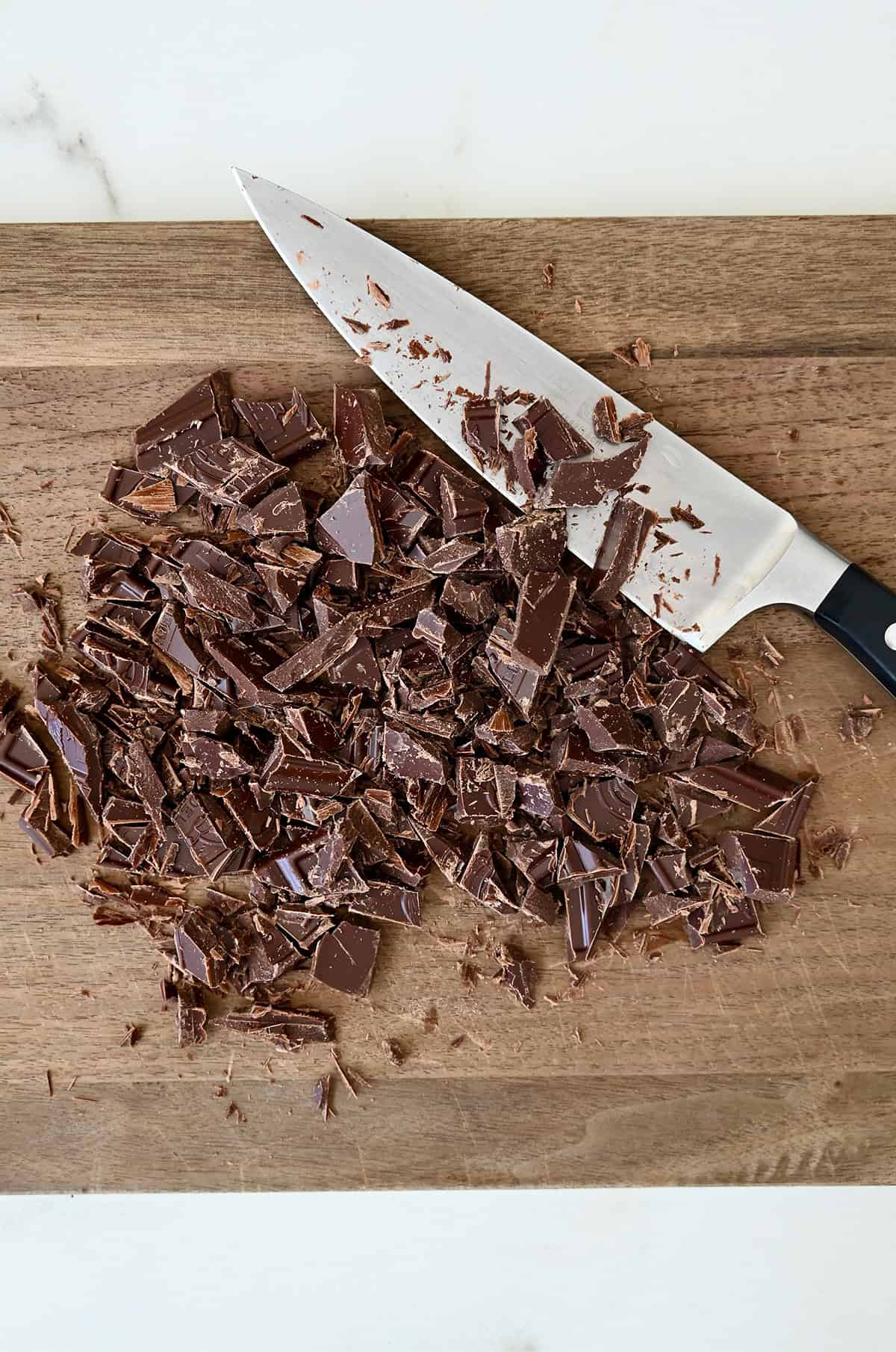 Chopped dark chocolate on a cutting board with a sharp knife.