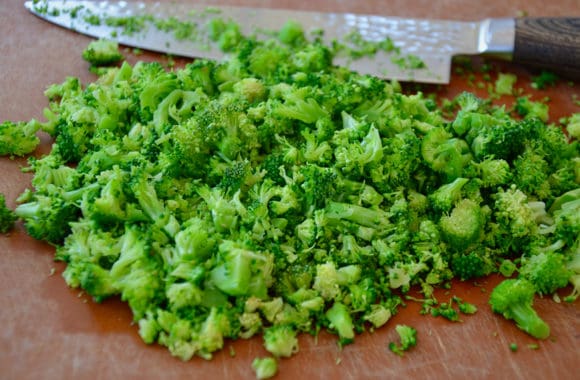 A wood cutting board with chopped broccoli and a knife