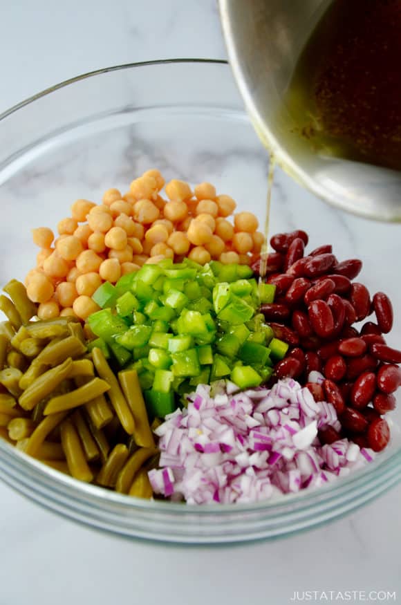 A class bowl containing beans, peppers and onions with dressing being poured in