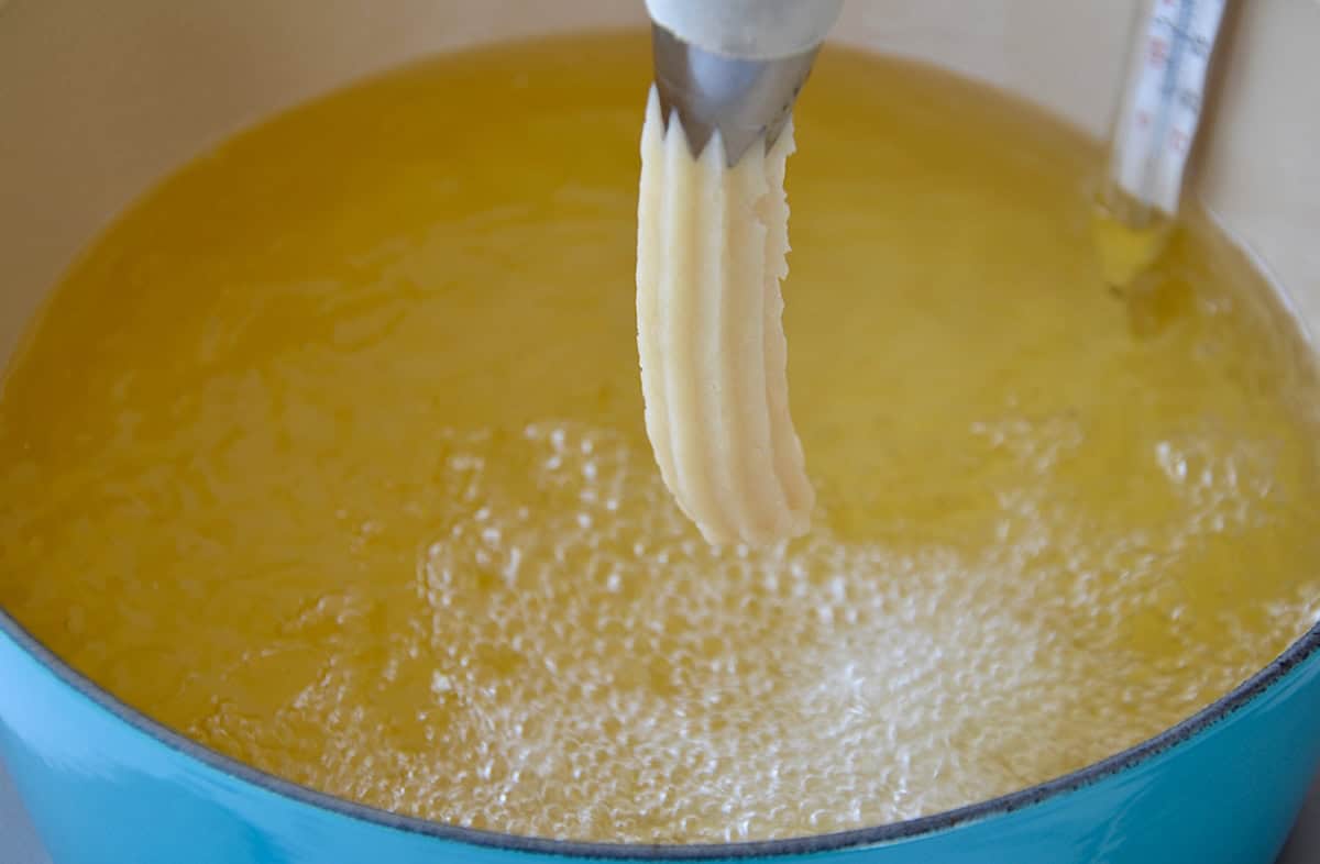 Piping churro dough into a heavy-bottomed stockpot filled with oil.