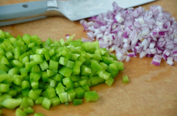 A cutting board with diced green peppers and red onion on top