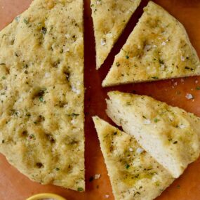 Four slices of Easy Homemade Focaccia (No Yeast) next to small bowls containing kosher salt and olive oil