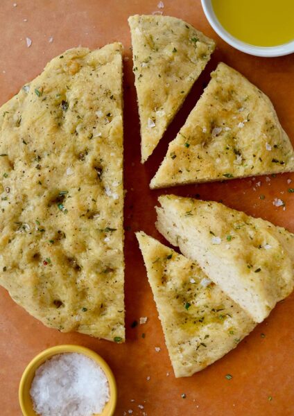 Four slices of Easy Homemade Focaccia (No Yeast) next to small bowls containing kosher salt and olive oil