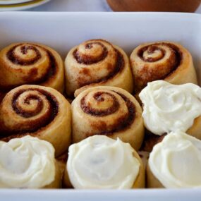 A white baking dish with cinnamon rolls and a bowl of frosting