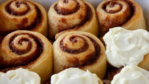 A white baking dish with cinnamon rolls and a bowl of frosting